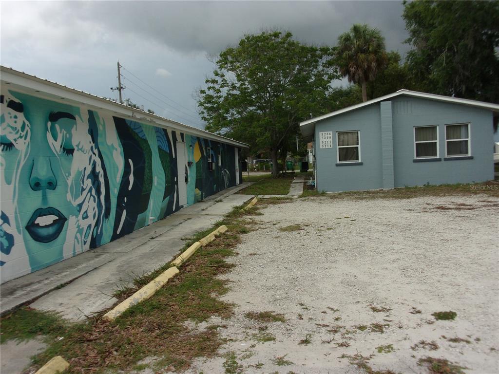 A mural-covered building stands next to a light blue house with a gravel parking area — 5208 7TH STREET, ZEPHYRHILLS, FL
