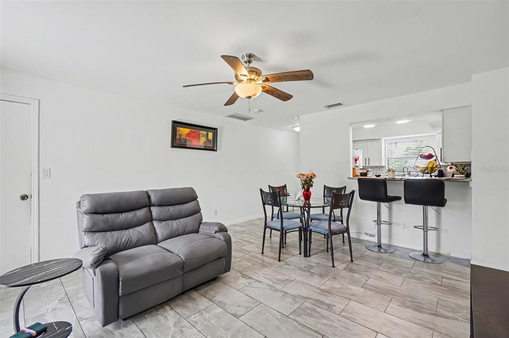 A living and dining area with gray tile floors, a gray sofa, and a kitchen pass-through — 2208/2210 IRIS WAY, FORT MYERS, FL