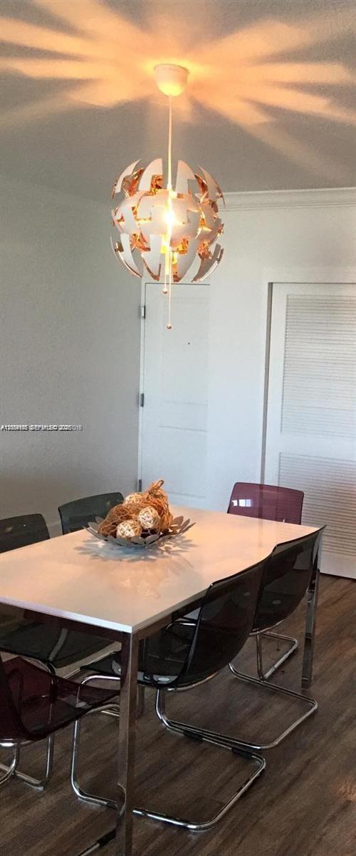 A dining room features a modern white and copper pendant light above a white table — 401 69th St # 905, Miami Beach FL 33141, MIAMI BEACH, FL