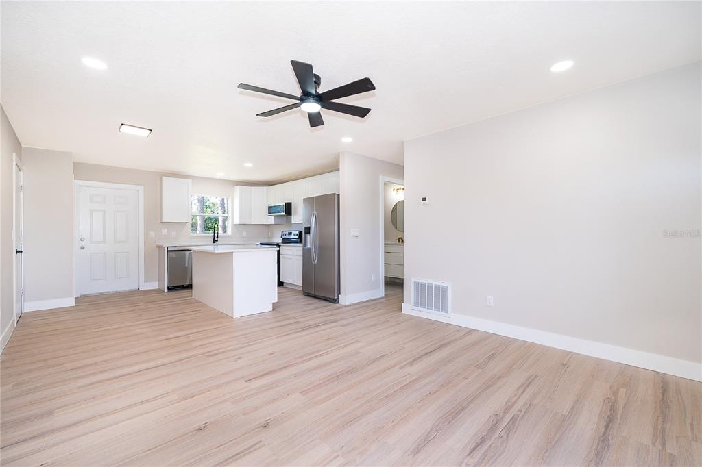 An open-concept kitchen and living area features light wood flooring, white cabinetry, and stainless appliances — 1033 EMBRUN COURT, KISSIMMEE, FL