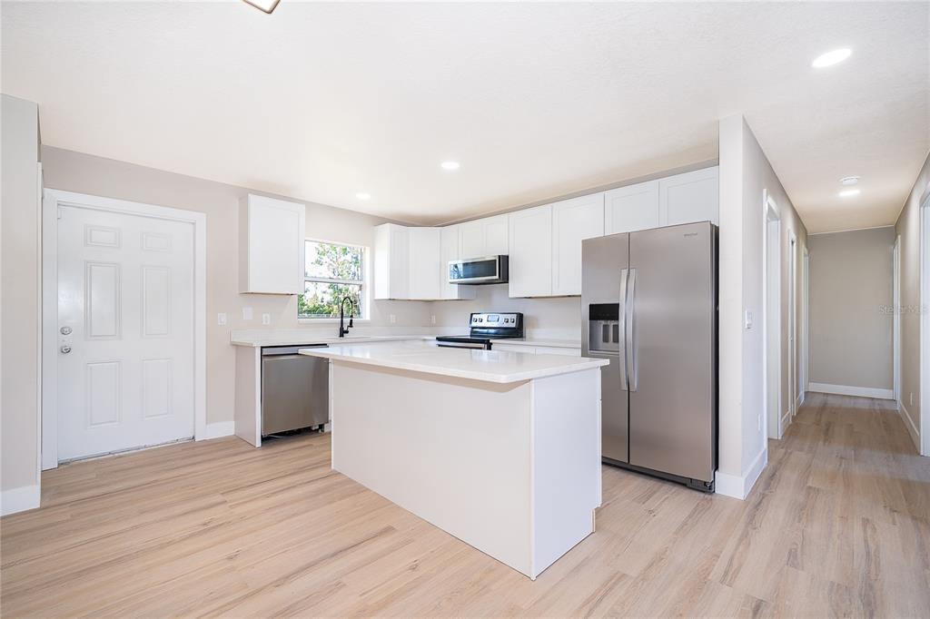 A modern kitchen features white cabinets, stainless steel appliances, a central island, and light flooring — 1033 EMBRUN COURT, KISSIMMEE, FL