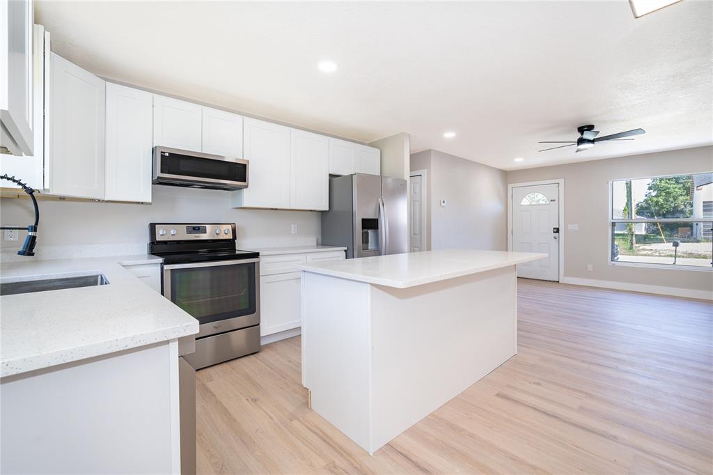 A kitchen with white cabinets, stainless steel appliances, and a central island with quartz countertops — 1033 EMBRUN COURT, KISSIMMEE, FL