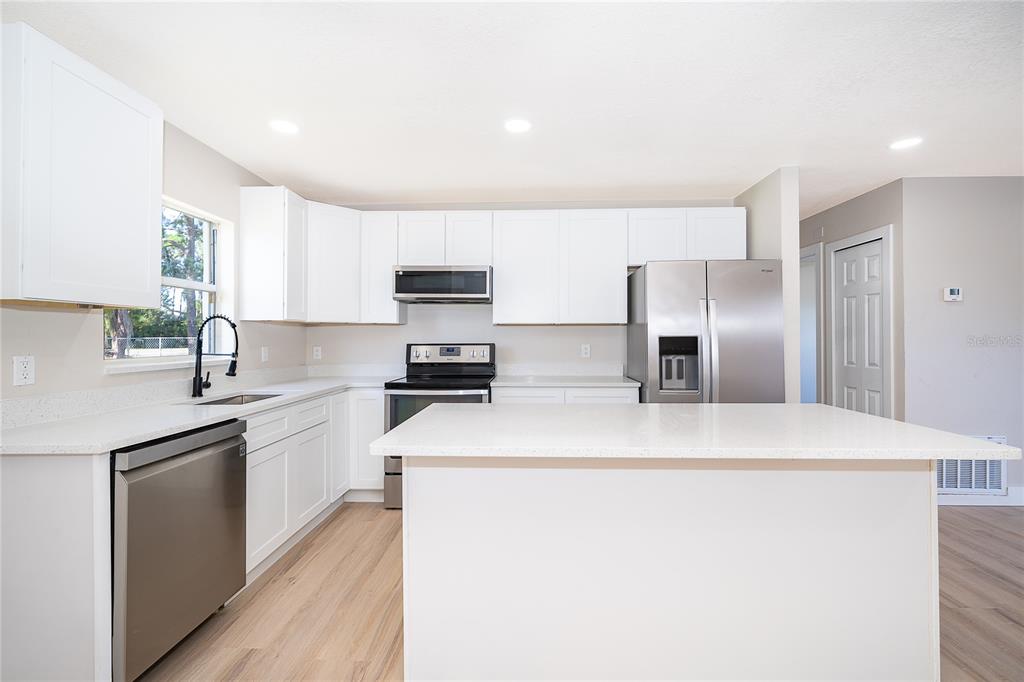 A modern kitchen features white cabinets, stainless steel appliances, and a central island with countertops — 1033 EMBRUN COURT, KISSIMMEE, FL