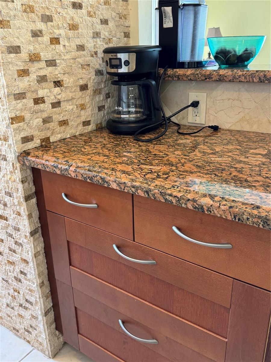 A kitchen counter features a coffee maker, granite countertops, and wood cabinets with metal pulls — 111 Briny Avenue # 11, Pompano Beach FL 33062, POMPANO BEACH, FL