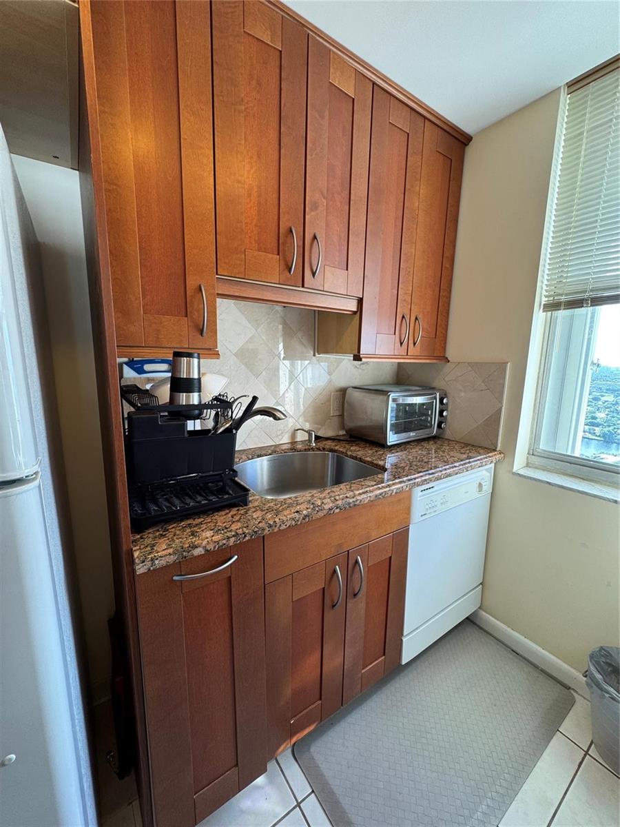 A small kitchen features cherry wood cabinets, granite countertops, a stainless steel sink, and dishwasher — 111 Briny Avenue # 11, Pompano Beach FL 33062, POMPANO BEACH, FL
