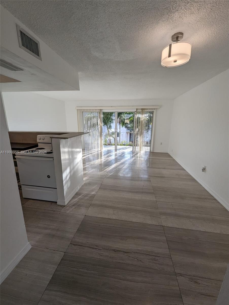 An open-concept living area features large light-colored floor tiles, a white stove, and sliding glass doors — 7360 SW 82nd St # E202, Miami FL 33143, MIAMI, FL