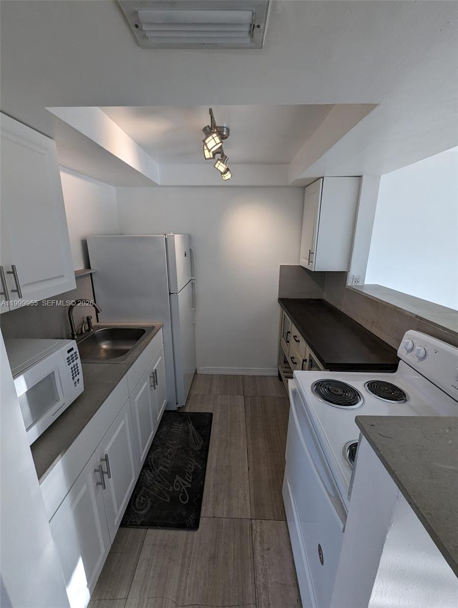 A galley-style kitchen features white cabinets, stainless steel appliances, and dark countertops — 7360 SW 82nd St # E202, Miami FL 33143, MIAMI, FL