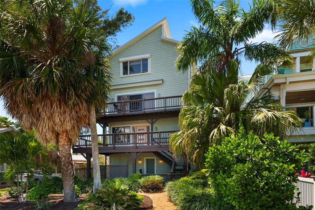 A three-story light green house with two wooden balconies and surrounding palm trees — 1304 PASS A GRILLE WAY, ST PETE BEACH, FL