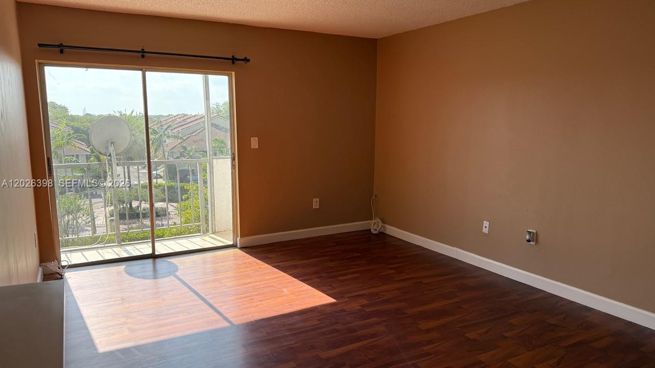 An empty room features dark wood-look flooring, tan walls, and a sliding glass balcony door — 8950 NE 8th Ave # 405, Miami FL 33138, MIAMI, FL
