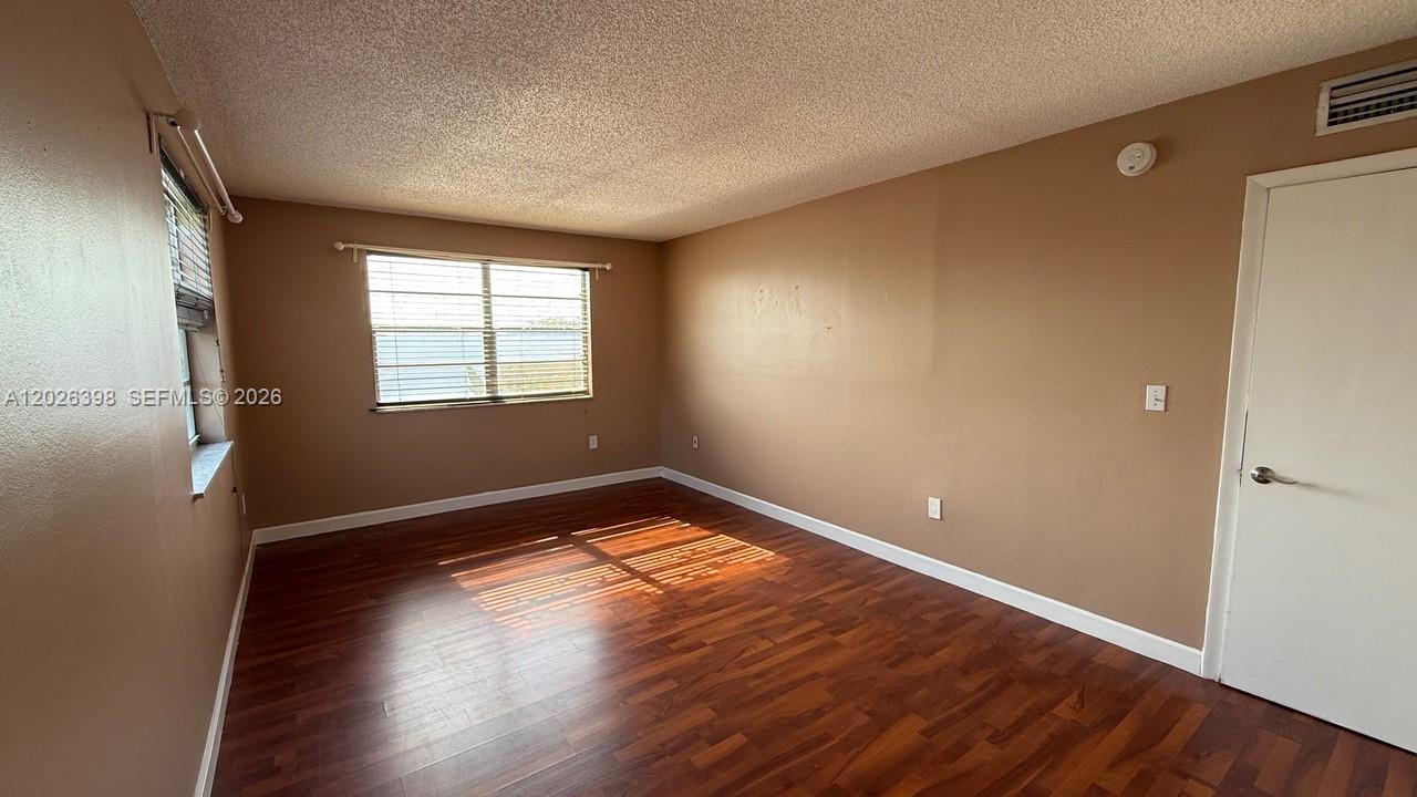 An empty bedroom features brown walls, wood-look flooring, and a window with blinds — 8950 NE 8th Ave # 405, Miami FL 33138, MIAMI, FL
