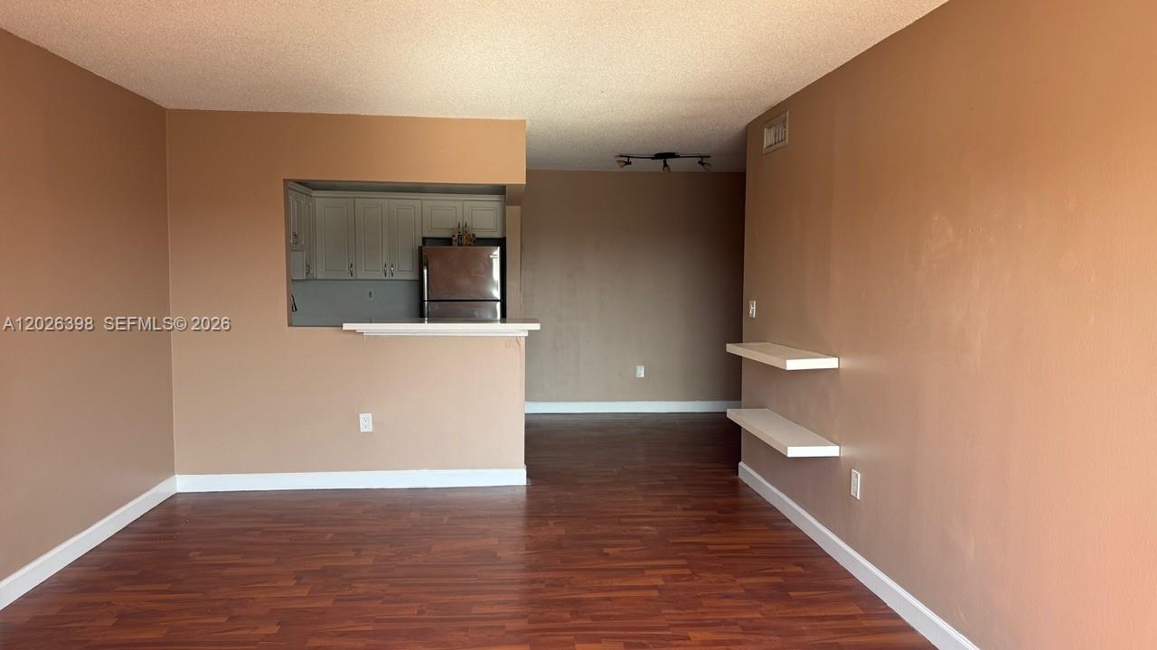 An empty living room features brown walls, dark wood-look flooring, and two white floating shelves — 8950 NE 8th Ave # 405, Miami FL 33138, MIAMI, FL