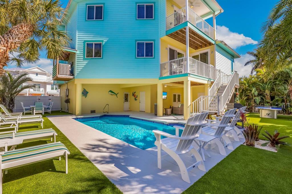 A bright blue and yellow stilt house features a swimming pool and patio seating area — 505 S BAY BOULEVARD, ANNA MARIA, FL