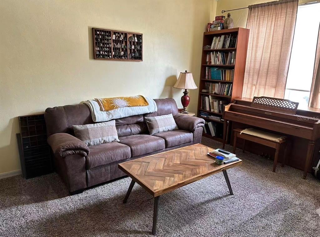 A living room features a brown sofa, a wooden coffee table, a bookshelf, and a piano — 3940 SW 20TH AVENUE UNIT 1107, GAINESVILLE, FL