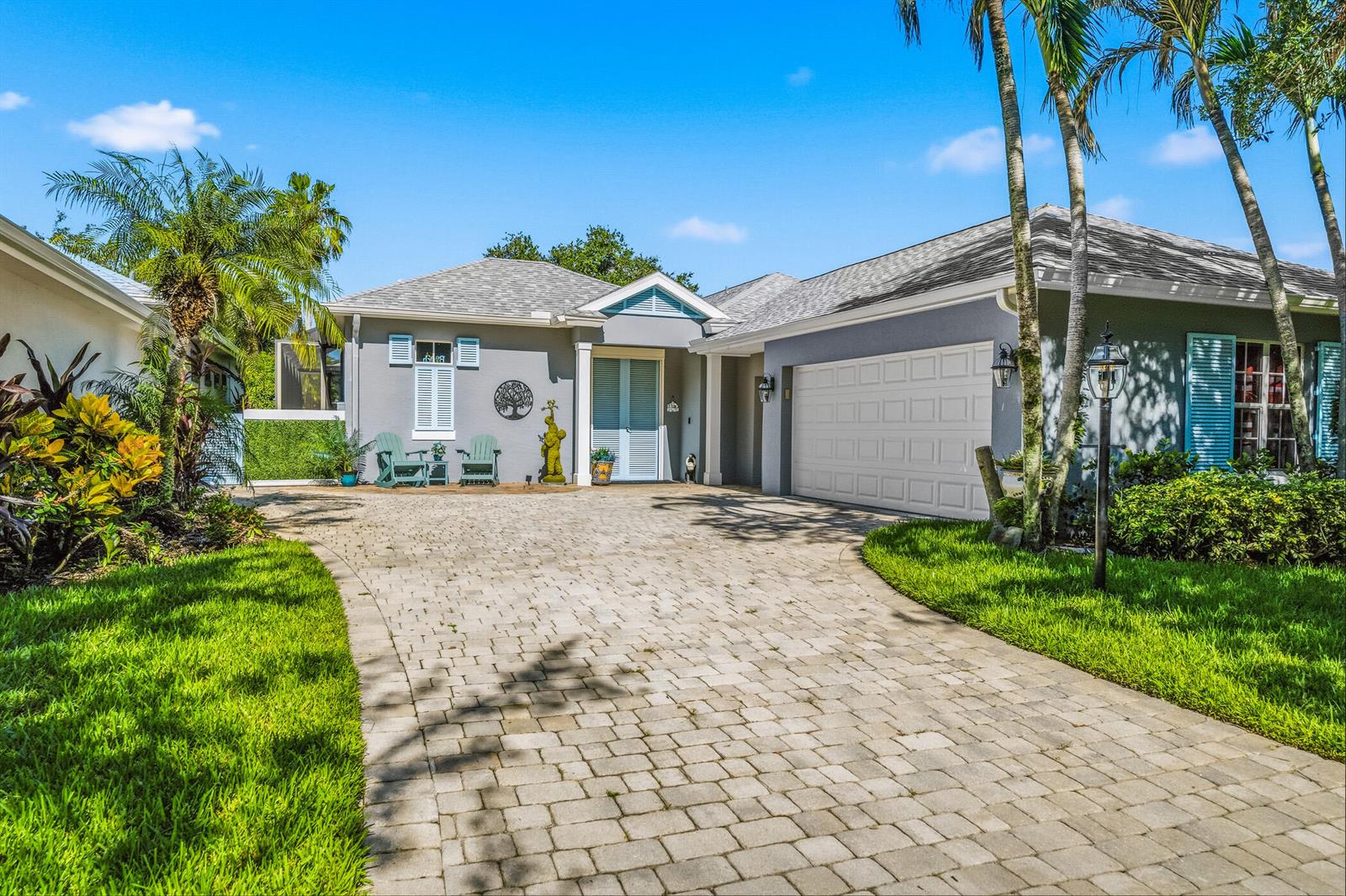 A gray single-story house with a paved driveway, white garage door, and blue shutters — 228 Oak Hammock Circle SW, Vero Beach FL 32962, VERO BEACH, FL