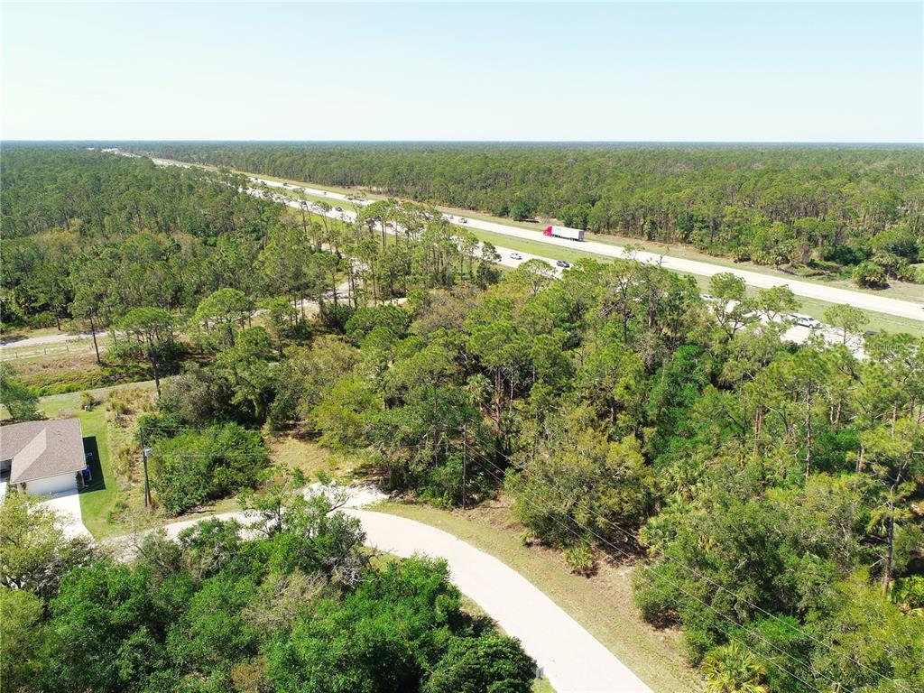 An aerial view shows a wooded lot adjacent to a highway with a nearby road — 8370 CHORLEY AVENUE, NORTH PORT, FL