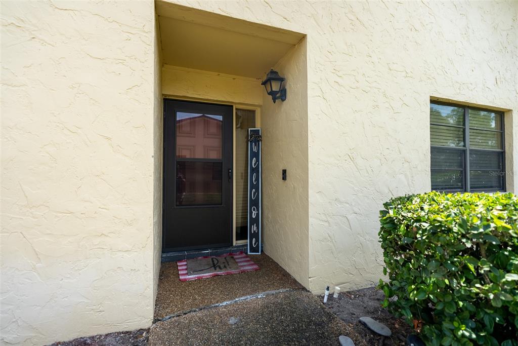 A front entrance with a dark storm door, a welcome sign, and a textured exterior wall — 1004 MEDINAH DRIVE, WINTER HAVEN, FL