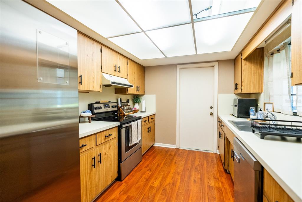 A kitchen with wood cabinets, stainless steel appliances, white countertops, and wood-look flooring — 1004 MEDINAH DRIVE, WINTER HAVEN, FL