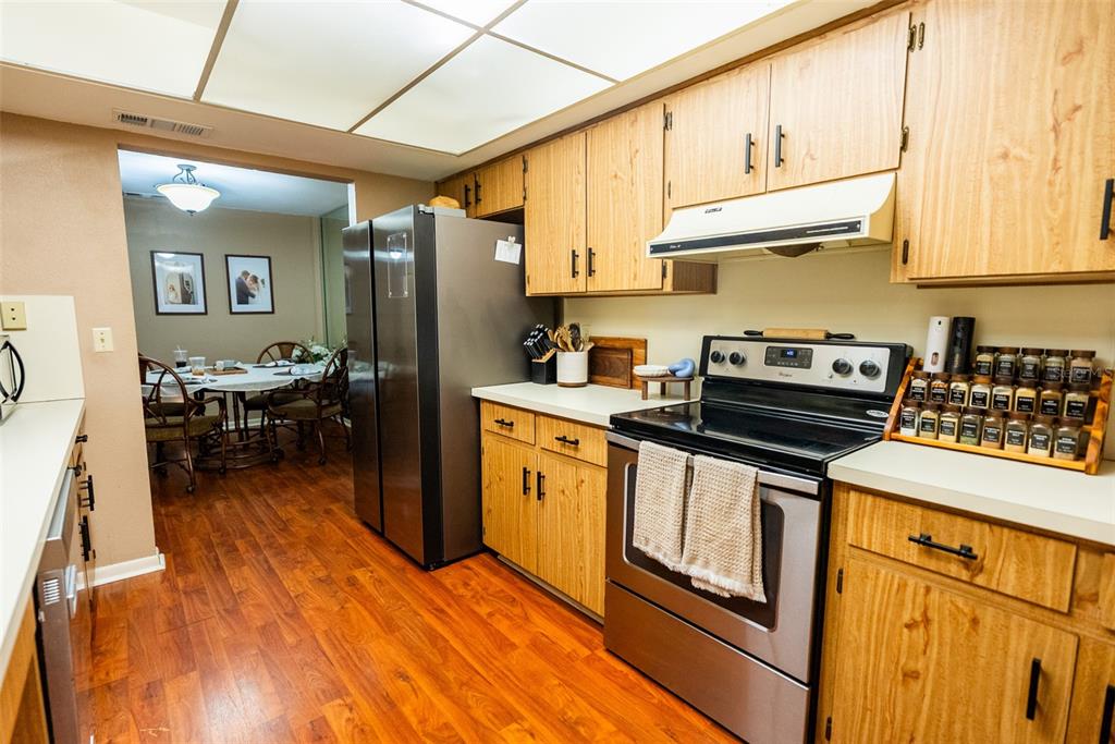 A kitchen with wood cabinets, stainless steel appliances, and wood flooring leads to a dining area — 1004 MEDINAH DRIVE, WINTER HAVEN, FL
