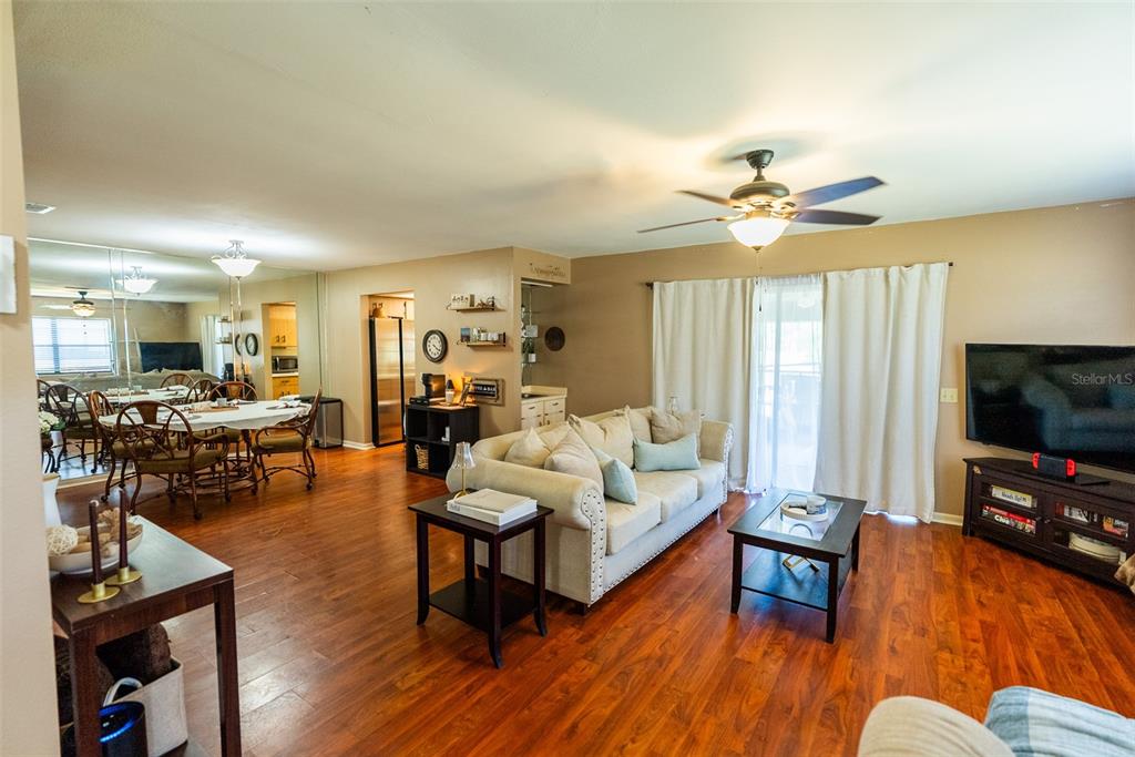A living room and dining area with hardwood floors, a beige sofa, and a ceiling fan — 1004 MEDINAH DRIVE, WINTER HAVEN, FL