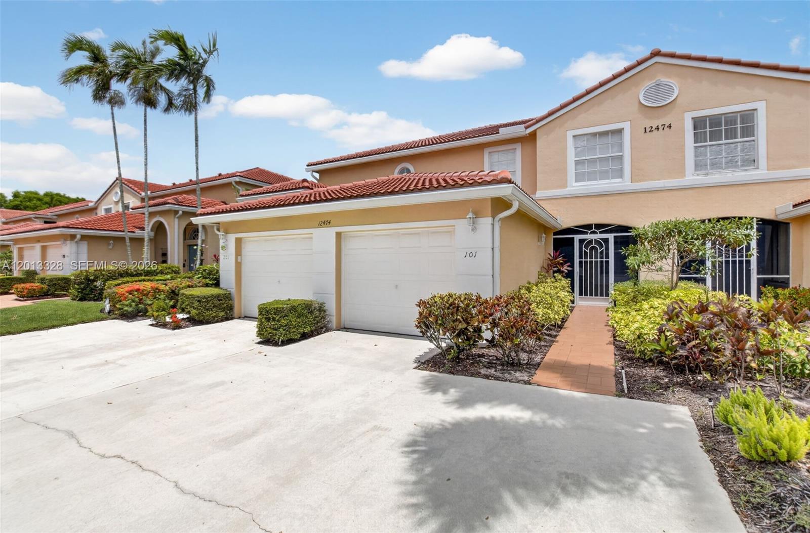 A two-story stucco townhouse features a two-car garage, a tiled roof, and a front walkway — 12474 Crystal Pointe Dr # 101, Boynton Beach FL 33437, BOYNTON BEACH, FL