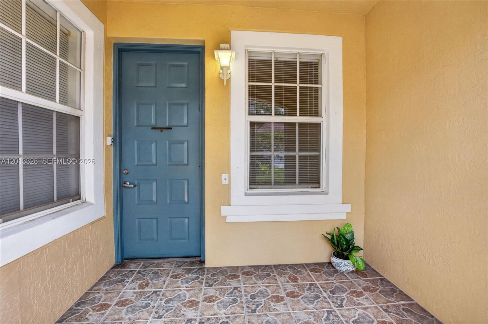 A blue front door is flanked by windows on a tiled porch with yellow walls — 12474 Crystal Pointe Dr # 101, Boynton Beach FL 33437, BOYNTON BEACH, FL