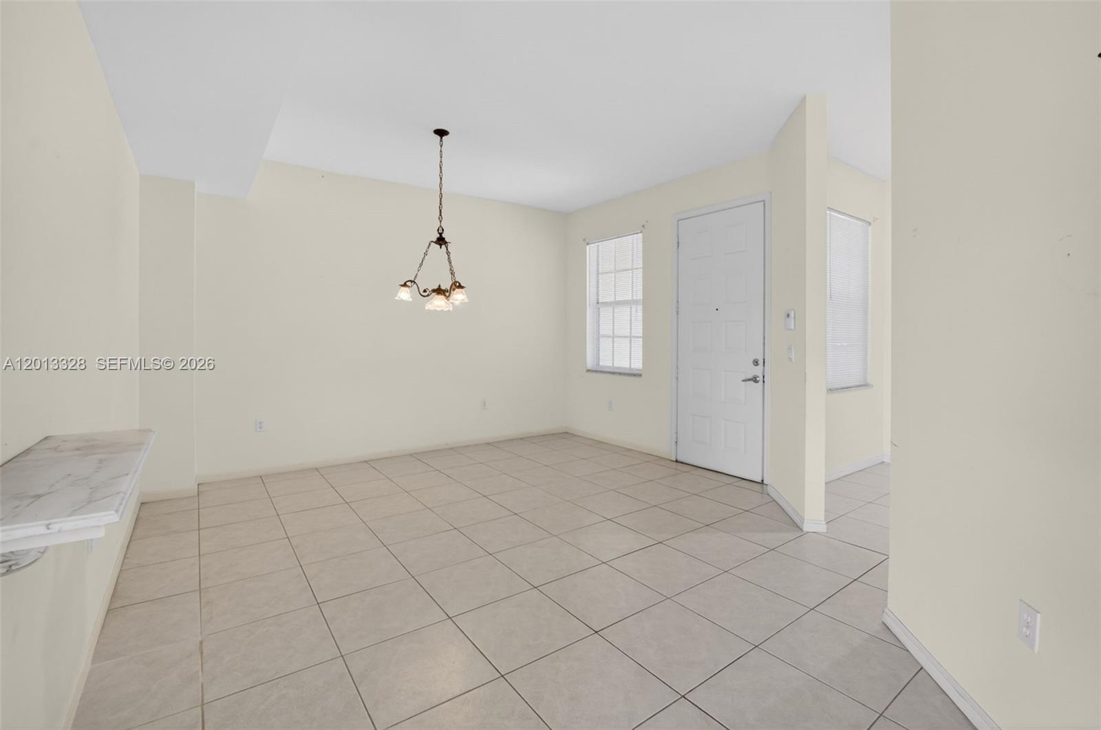 This room features light-colored tile flooring, a dining chandelier, and a white entry door — 12474 Crystal Pointe Dr # 101, Boynton Beach FL 33437, BOYNTON BEACH, FL