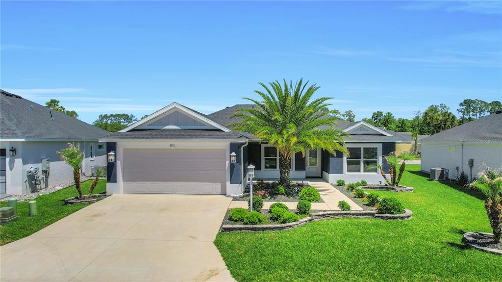 A single-story suburban house with a two-car garage, a palm tree, and landscaped front yard — 4151 BALCHARAN TERRACE, THE VILLAGES, FL