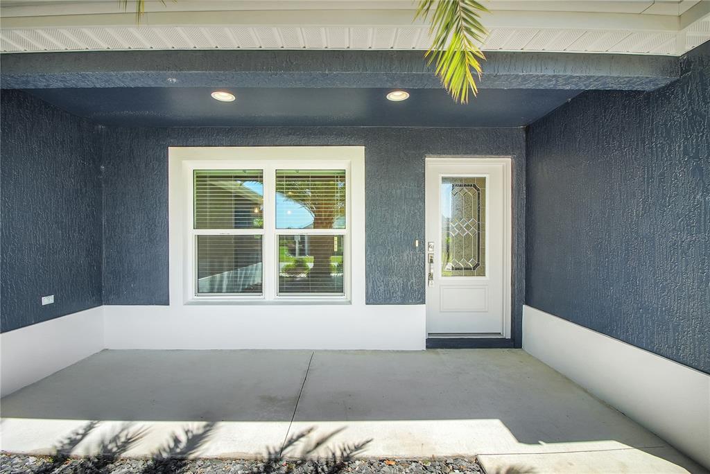 A covered concrete porch features dark blue textured walls, a white door, and a window — 4151 BALCHARAN TERRACE, THE VILLAGES, FL
