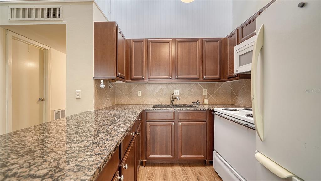A kitchen features dark wood cabinets, granite countertops, and white appliances — 500 N JEFFERSON AVENUE UNIT B-5, SARASOTA, FL