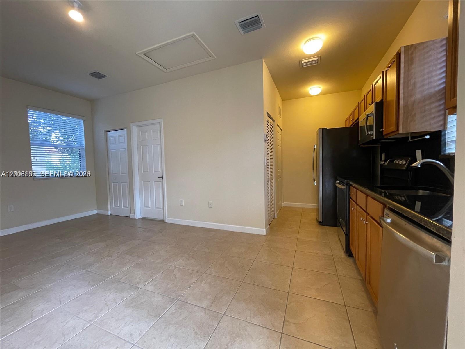 This kitchen features light tile flooring, wooden cabinets, black appliances, and a window with blinds — 9351 SW 171st Ave, Miami FL 33196, MIAMI, FL