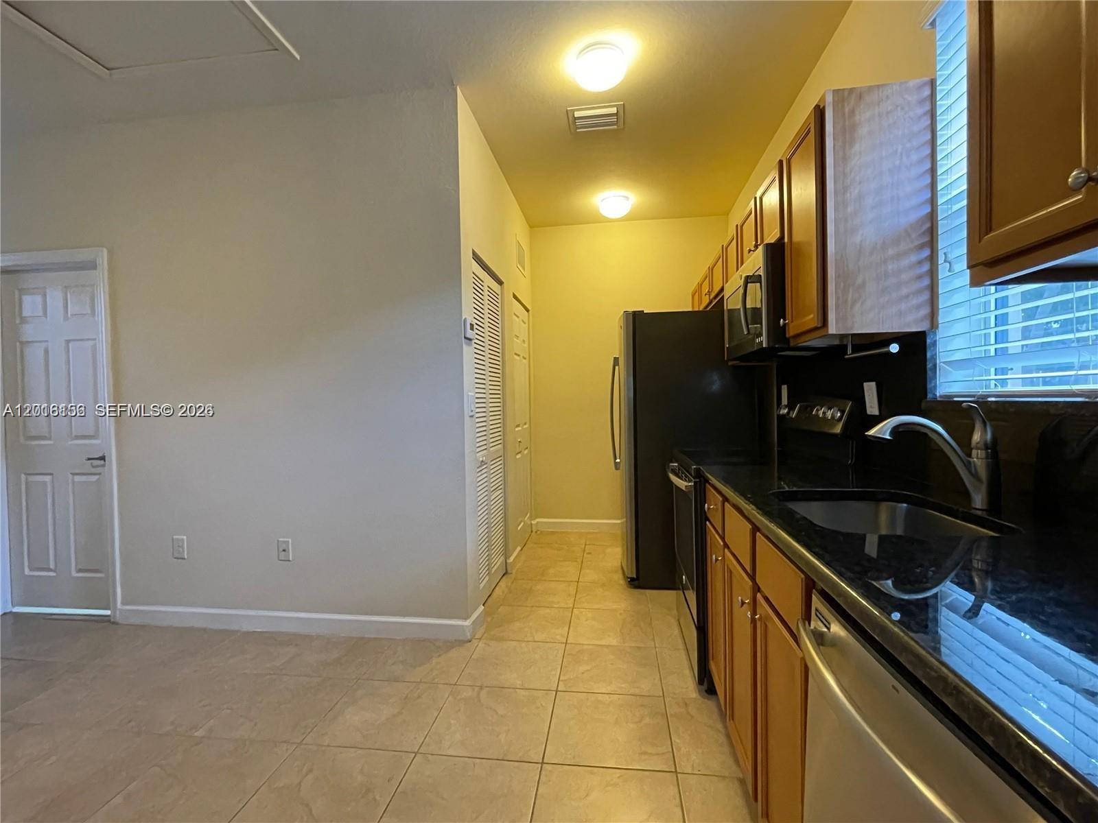 A kitchen features wood cabinets, black countertops, stainless steel appliances, and beige tile flooring — 9351 SW 171st Ave, Miami FL 33196, MIAMI, FL