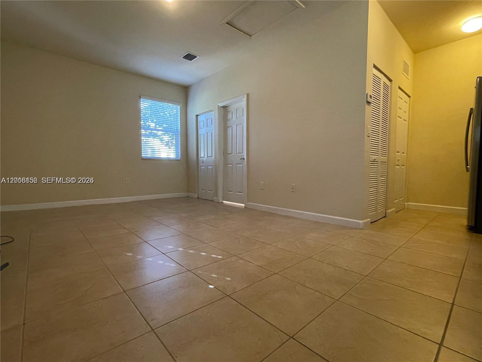 A room with beige tile flooring, light-colored walls, a window, and several interior doors — 9351 SW 171st Ave, Miami FL 33196, MIAMI, FL
