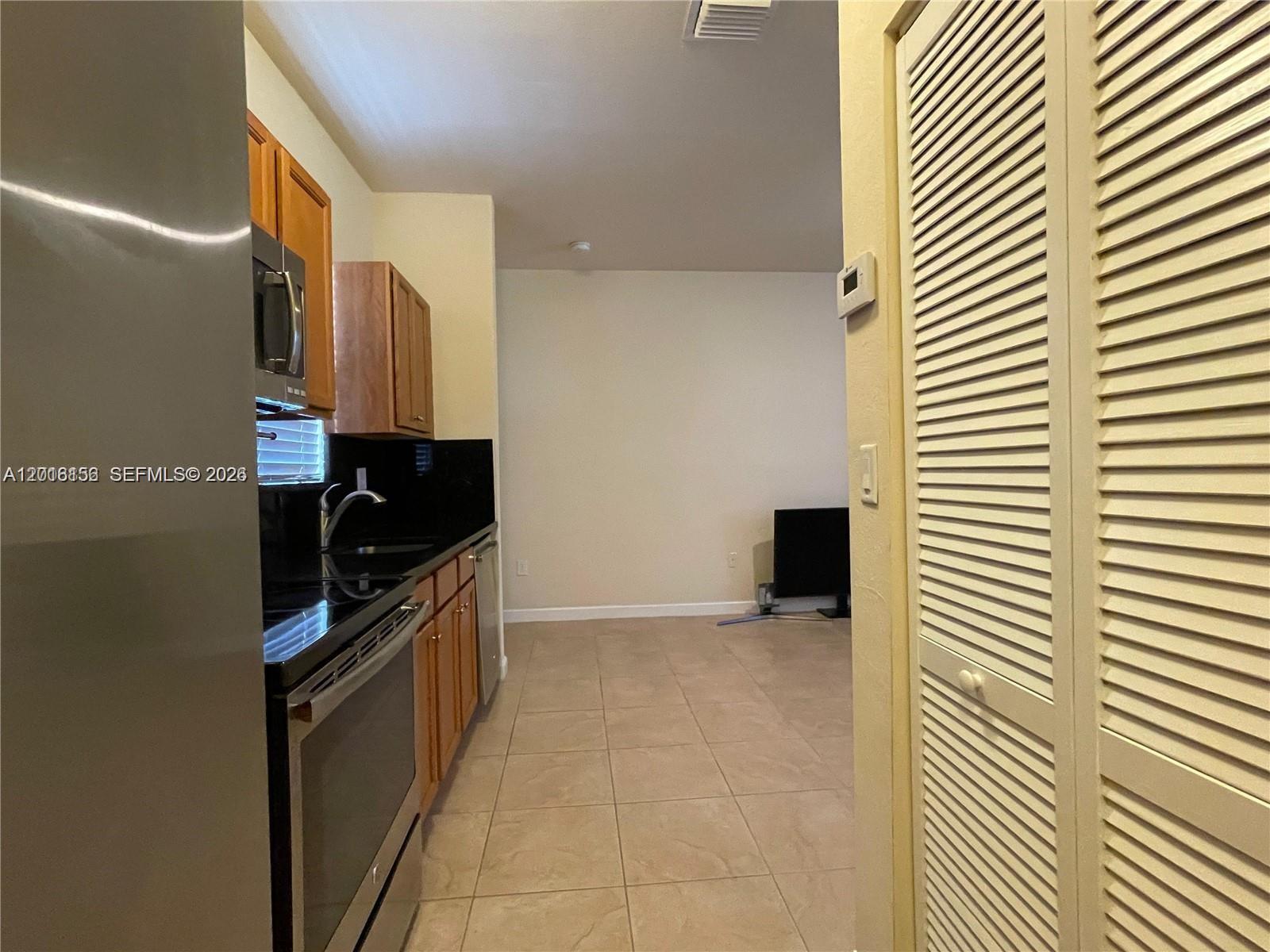 A kitchen with wooden cabinets, black countertops, and tile flooring opens into a living area — 9351 SW 171st Ave, Miami FL 33196, MIAMI, FL