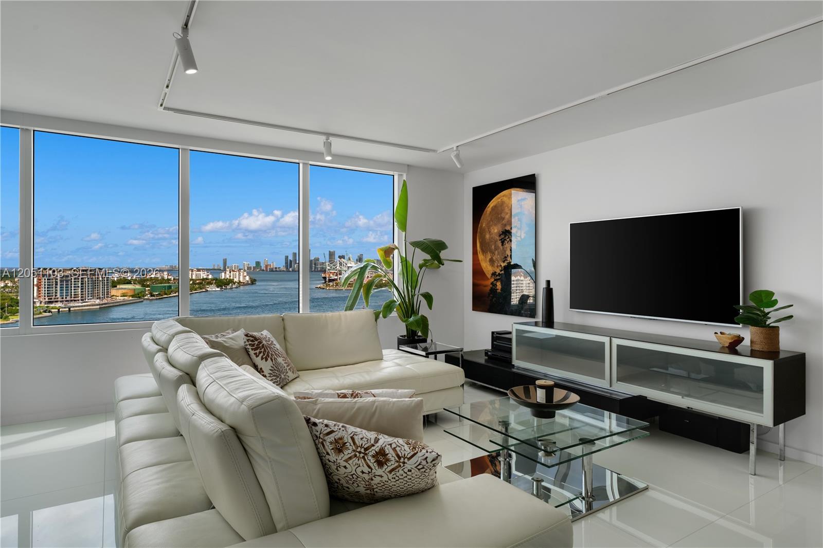 A modern living room features a white sectional sofa, glass coffee table, and waterfront city views — 400 S Pointe Dr # 1805, Miami Beach FL 33139, MIAMI BEACH, FL