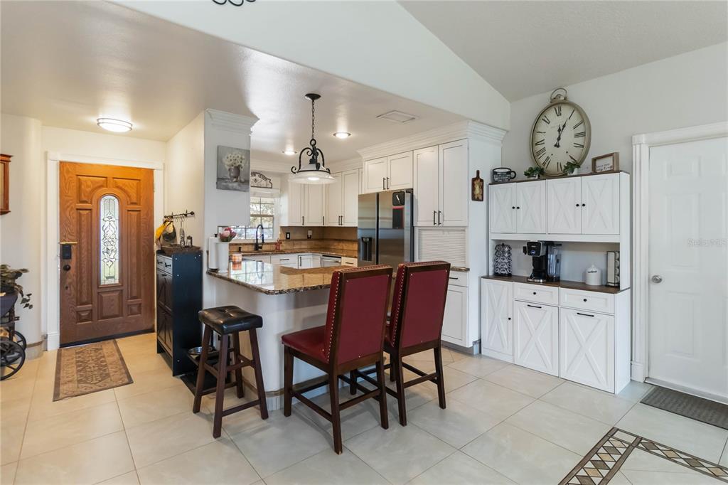 A kitchen features white cabinetry, granite countertops, a breakfast bar with two chairs, and tile flooring — 439 VIRGINIA AVENUE, ST CLOUD, FL