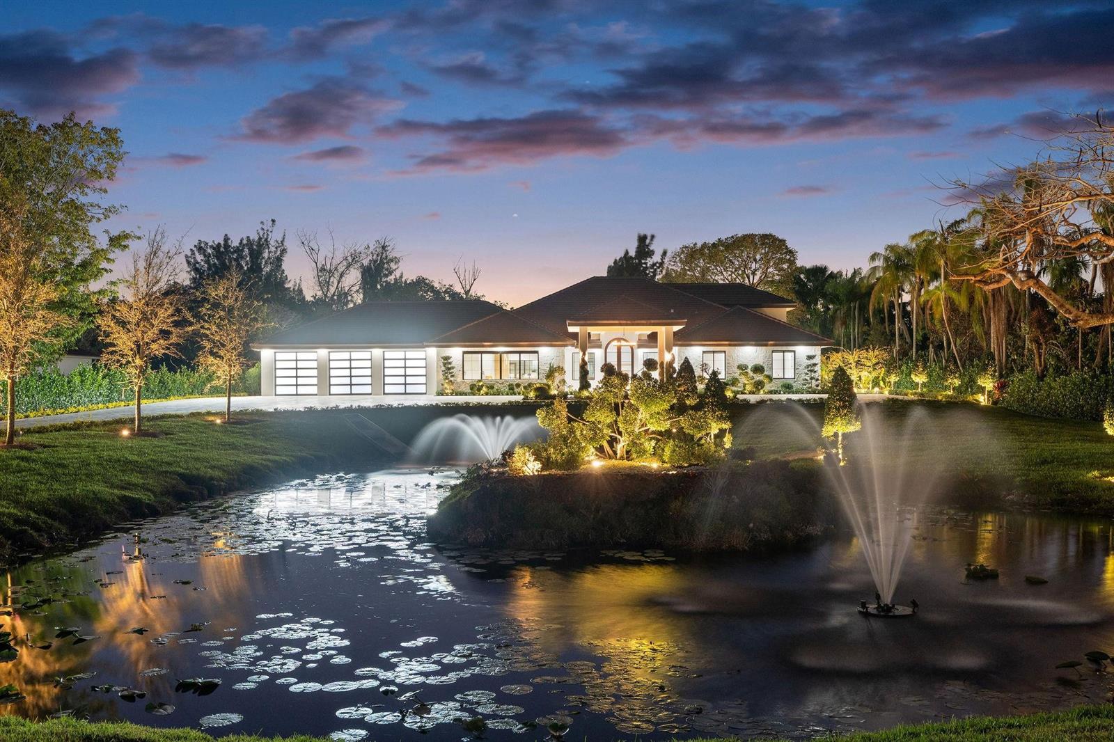 A large, single-story house with a three-car garage sits behind a pond with two fountains — 13110 Mustang Trail, Southwest Ranches FL 33330, SOUTHWEST RANCHES, FL
