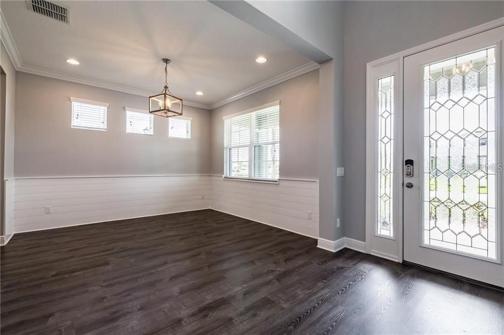 An empty dining room features white shiplap wainscoting, dark wood flooring, and a glass-paneled front door — 11301 ALACHUA CREEK LANE, RIVERVIEW, FL