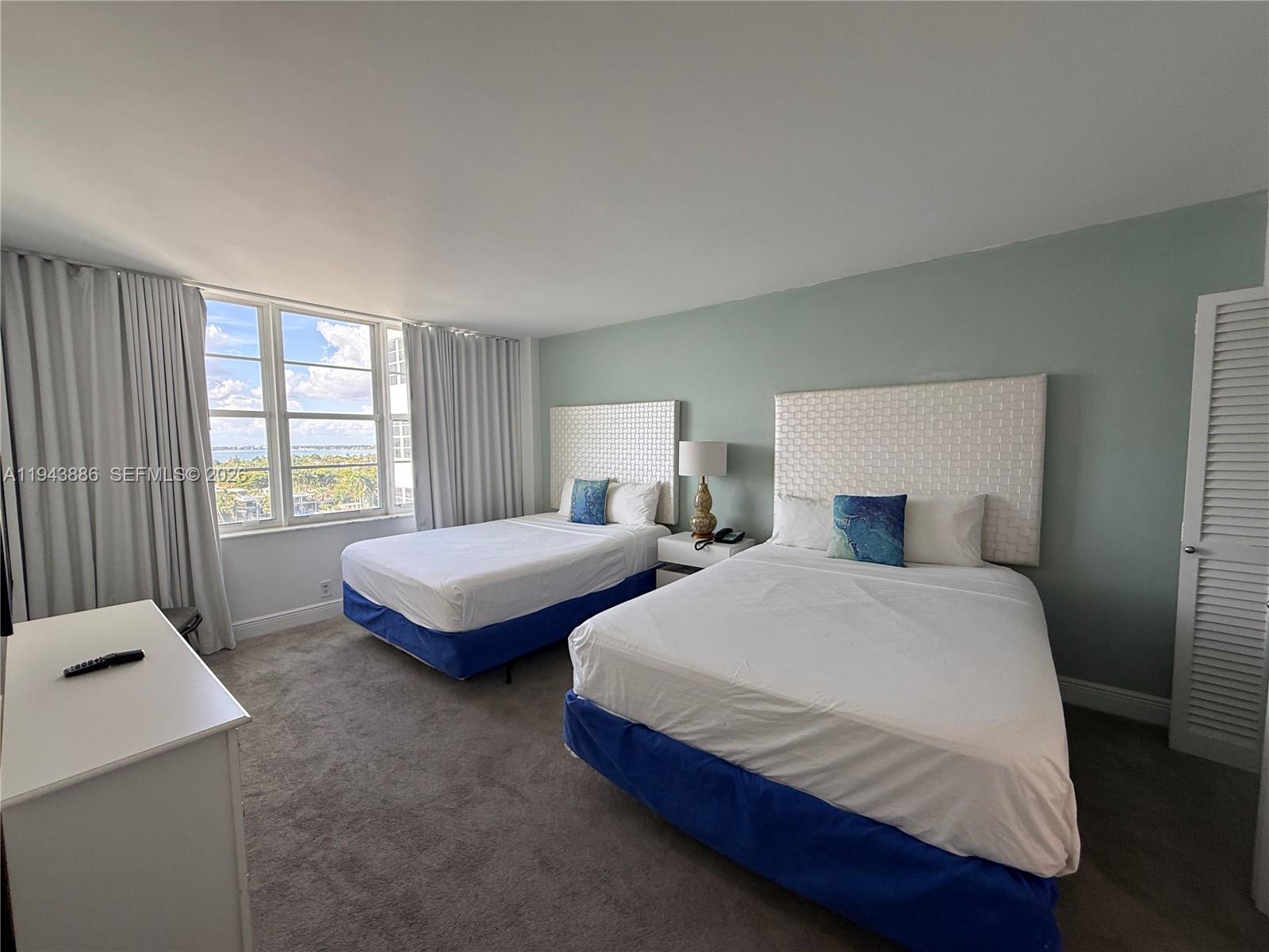 A hotel-style bedroom features two beds with white headboards and a view of the water — 5101 Collins Ave # 12T, Miami Beach FL 33140, MIAMI BEACH, FL