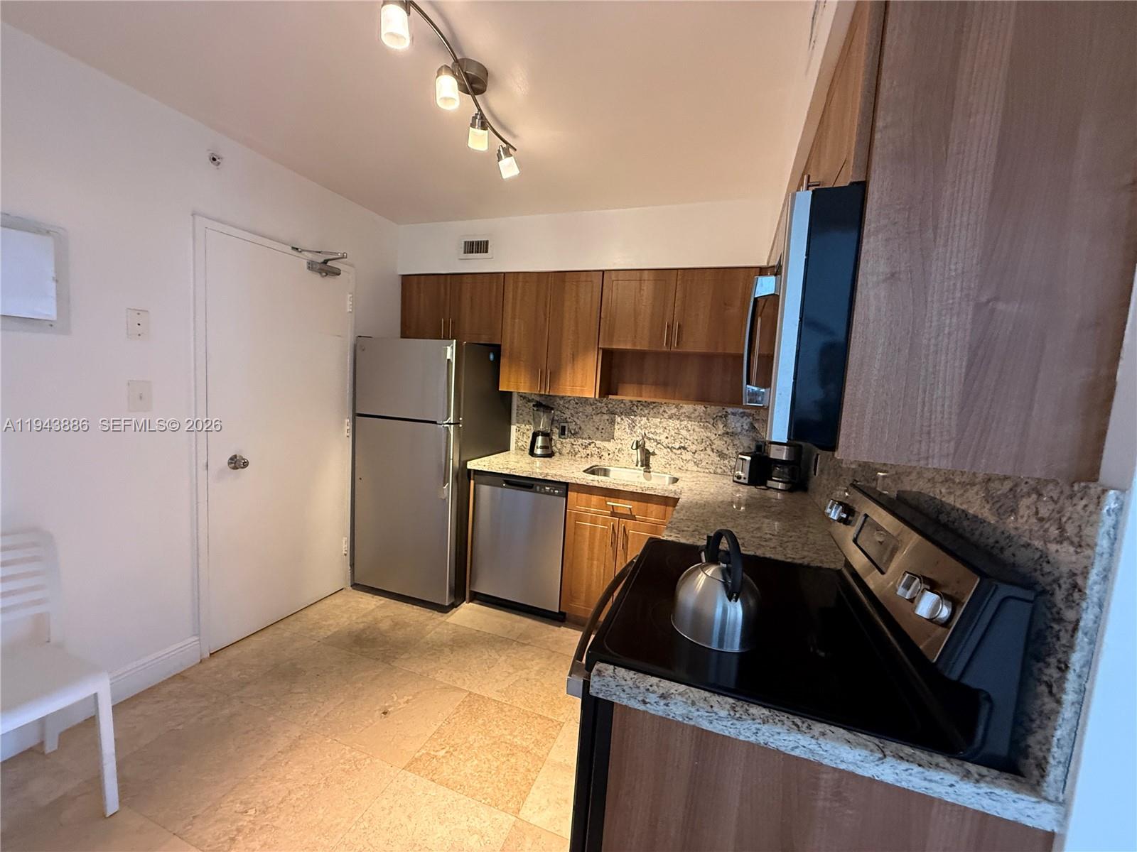 A kitchen features wood cabinets, stainless steel appliances, granite countertops, and tile flooring — 5101 Collins Ave # 12T, Miami Beach FL 33140, MIAMI BEACH, FL