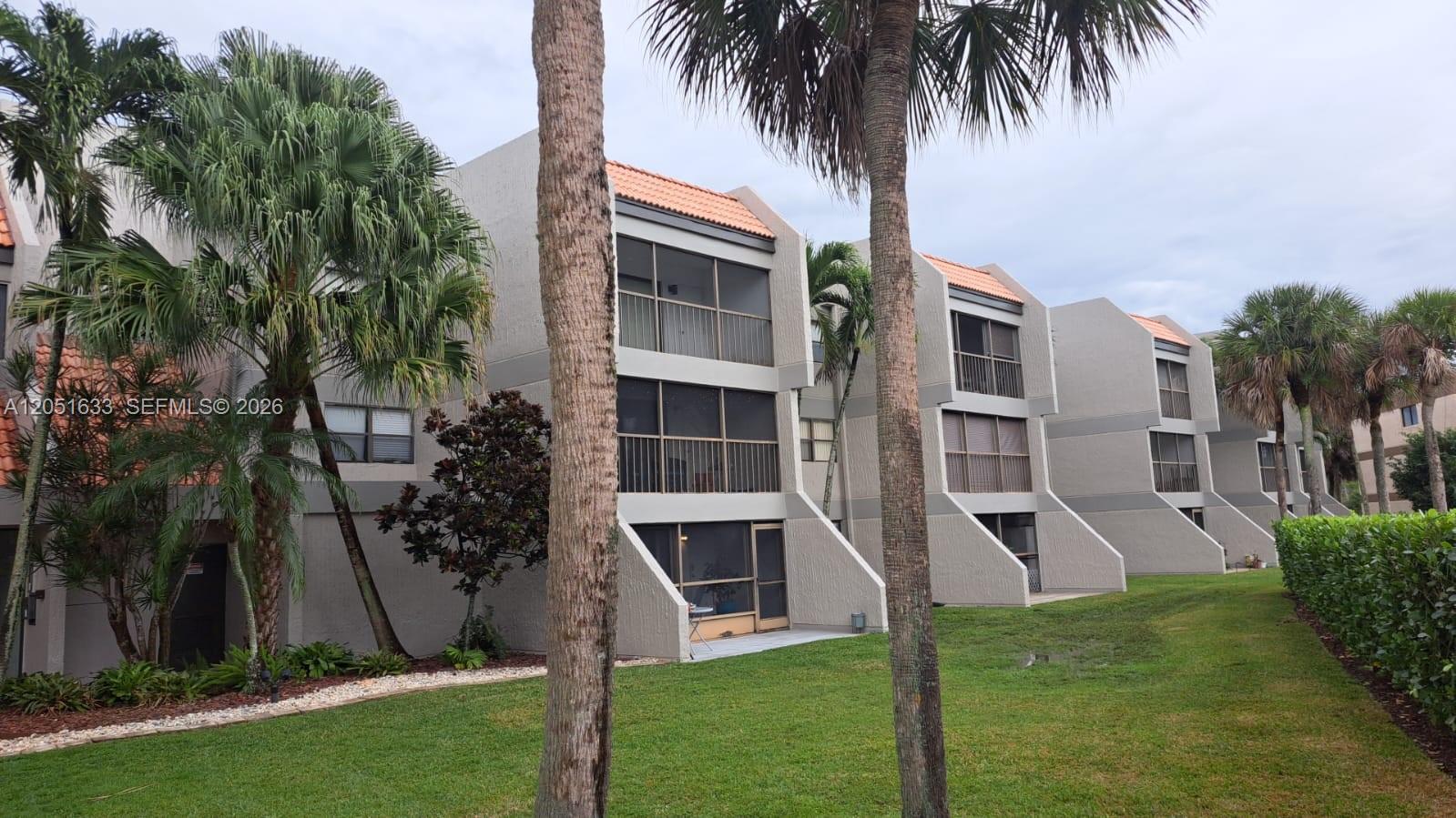 The exterior of a multi-story apartment complex features screened balconies and palm trees — 230 Lakeview Dr # 310, Weston FL 33326, WESTON, FL