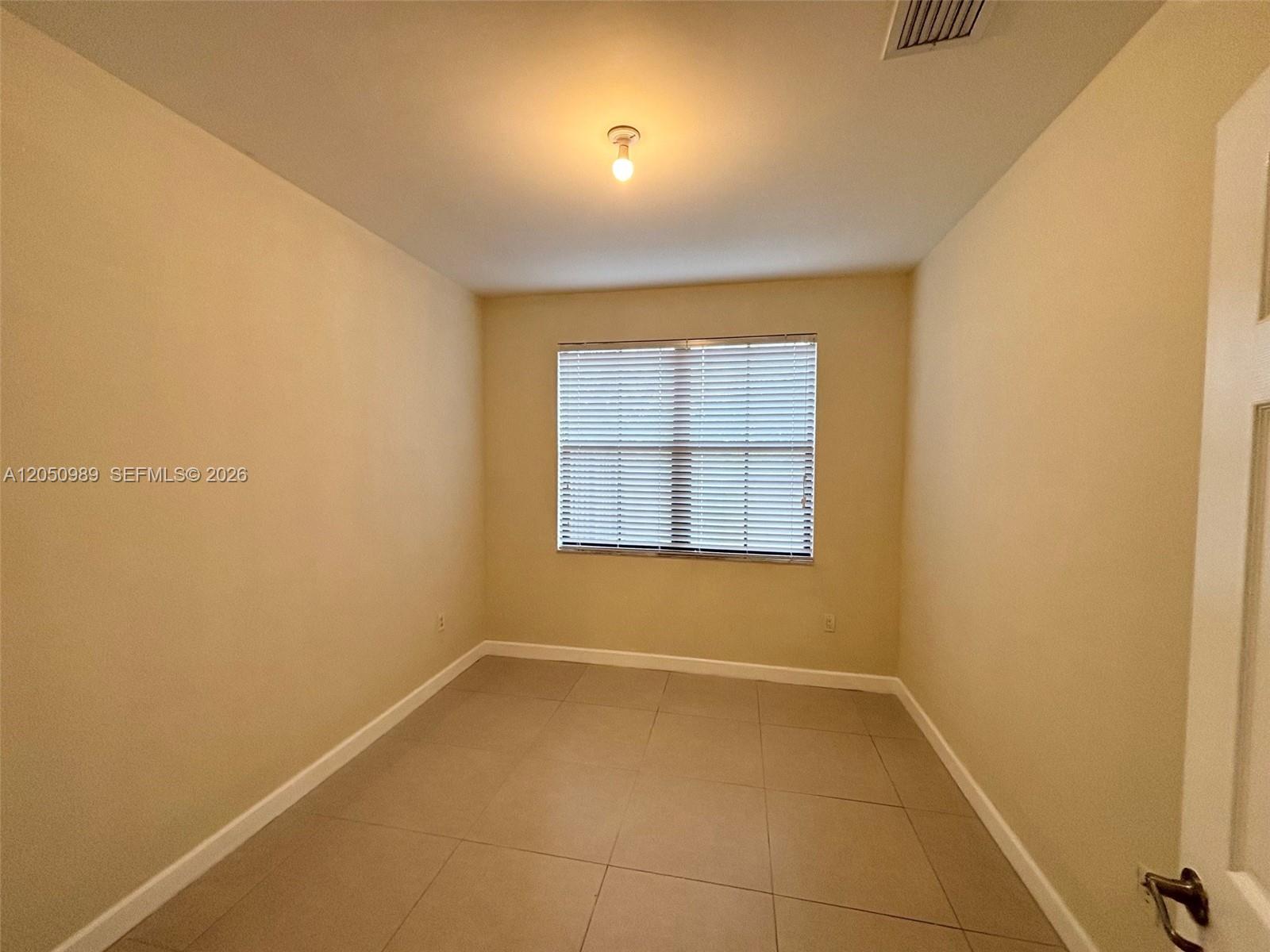 An empty room features beige walls, light-colored tile flooring, and a single window with blinds — 10445 NW 61 LN # 10445, Doral FL 33178, DORAL, FL