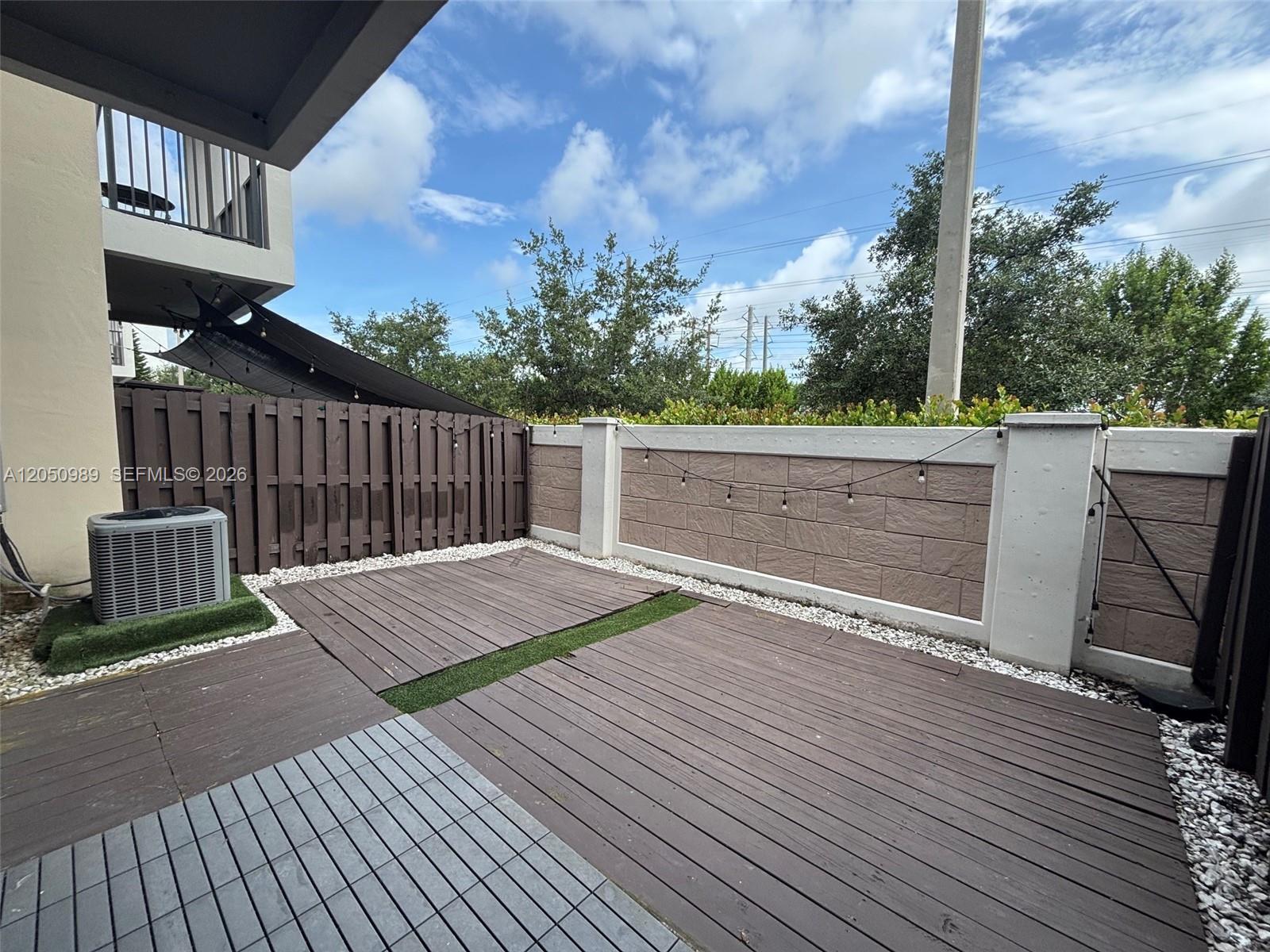A fenced outdoor patio features wooden decking, artificial turf strips, and a central air conditioning unit — 10445 NW 61 LN # 10445, Doral FL 33178, DORAL, FL