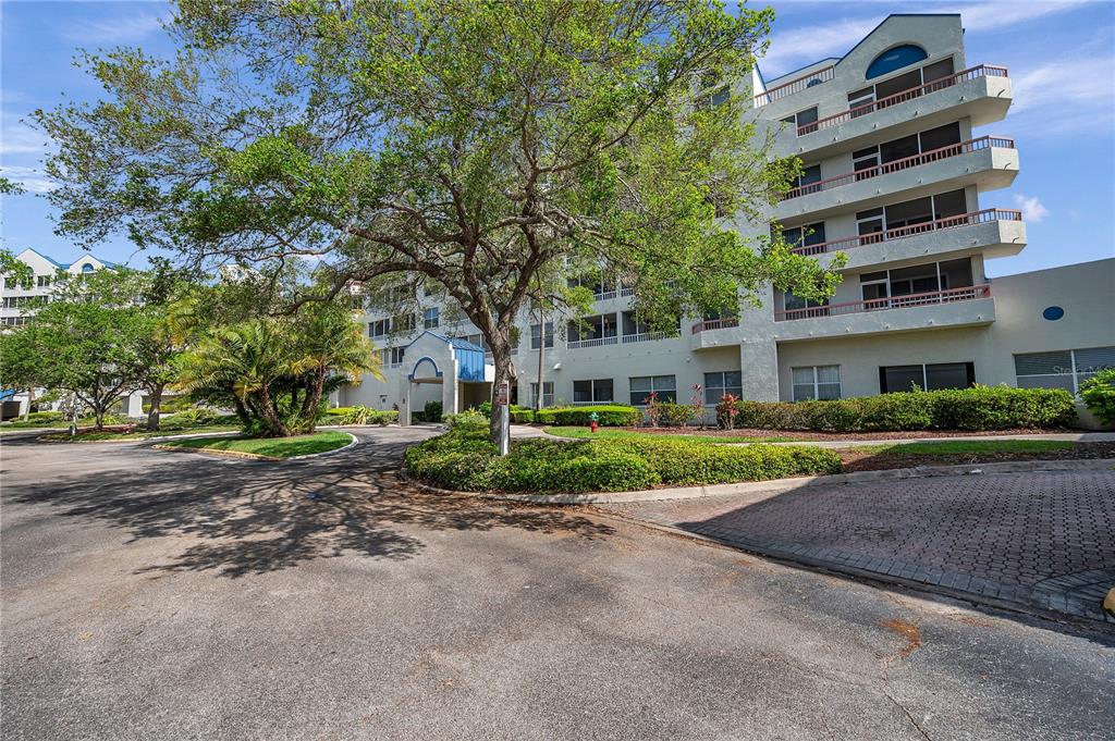 A multi-story apartment building with balconies stands behind a large tree and paved driveway — 2333 FEATHER SOUND DRIVE UNIT B307, CLEARWATER, FL