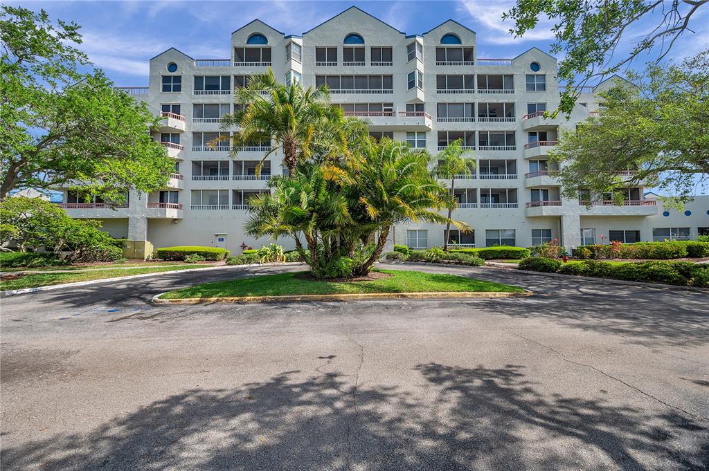 A multi-story residential building with screened balconies stands behind a circular driveway and palm trees — 2333 FEATHER SOUND DRIVE UNIT B307, CLEARWATER, FL