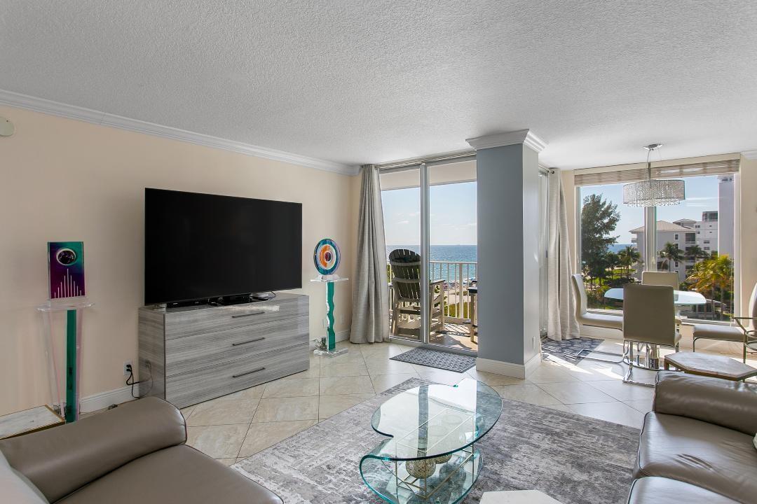A living room with a television, glass coffee table, and floor-to-ceiling windows overlooking the ocean — 1010 S Ocean Boulevard # 602, Pompano Beach FL 33062, POMPANO BEACH, FL