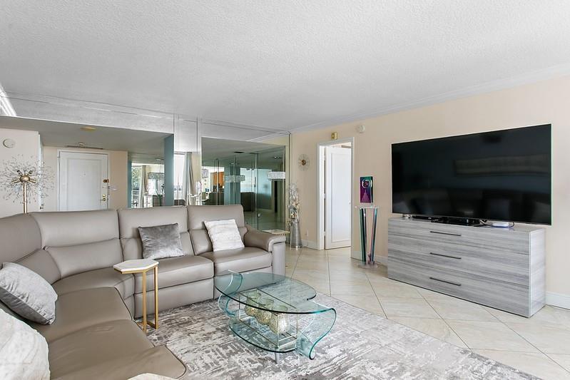 A living room features a gray leather sectional, a glass coffee table, and a large television — 1010 S Ocean Boulevard # 602, Pompano Beach FL 33062, POMPANO BEACH, FL