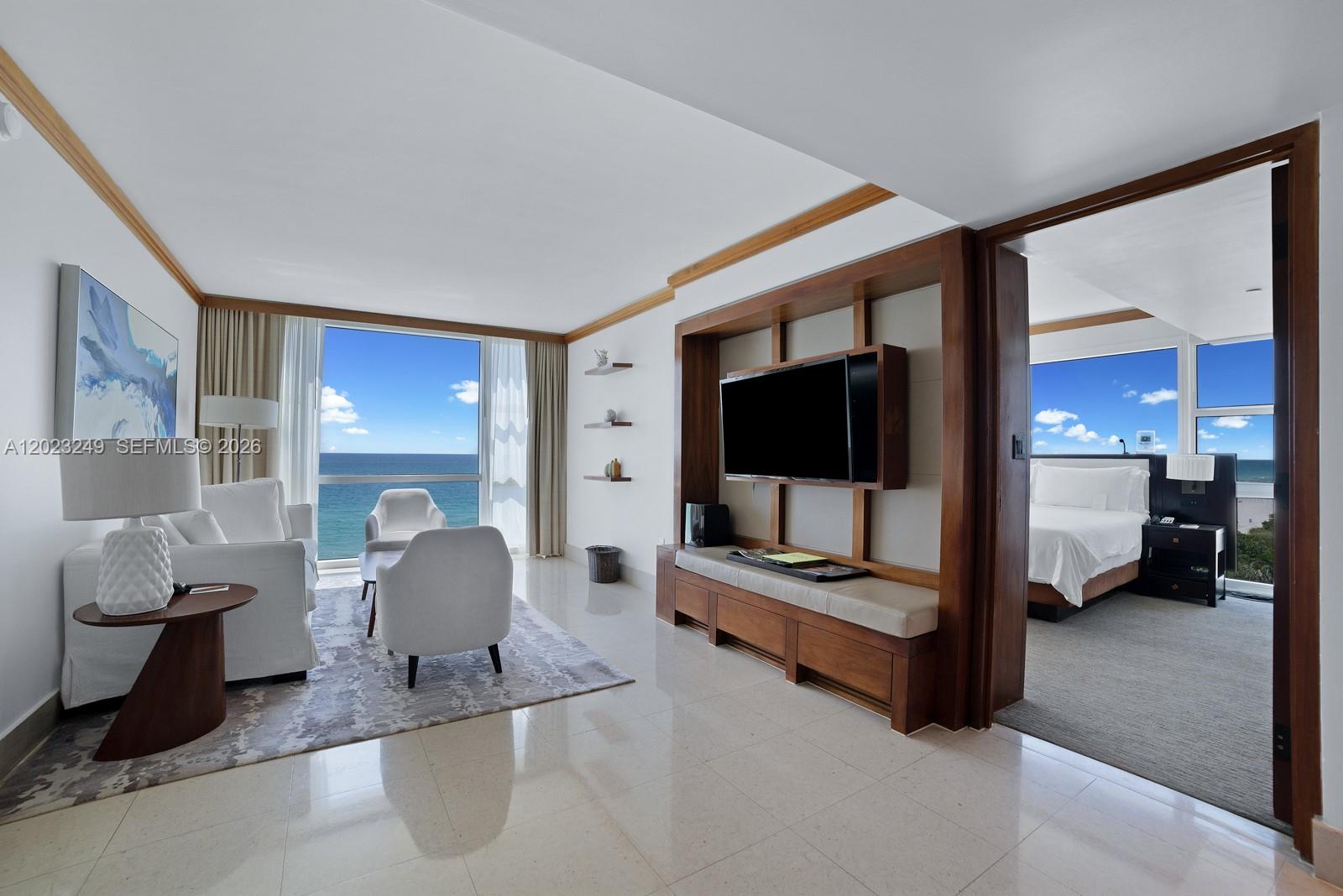 A living room with ocean views leads into a bedroom through a wooden doorway — 6801 Collins Ave, Miami Beach FL 33141, MIAMI BEACH, FL