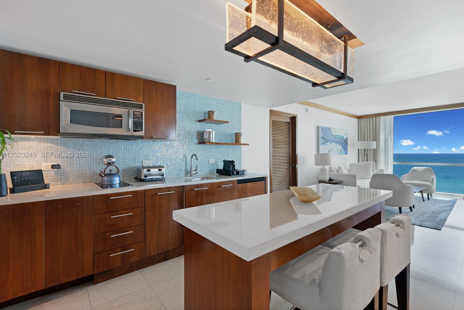 A modern kitchen with wood cabinets and a white island overlooks the ocean view — 6801 Collins Ave, Miami Beach FL 33141, MIAMI BEACH, FL