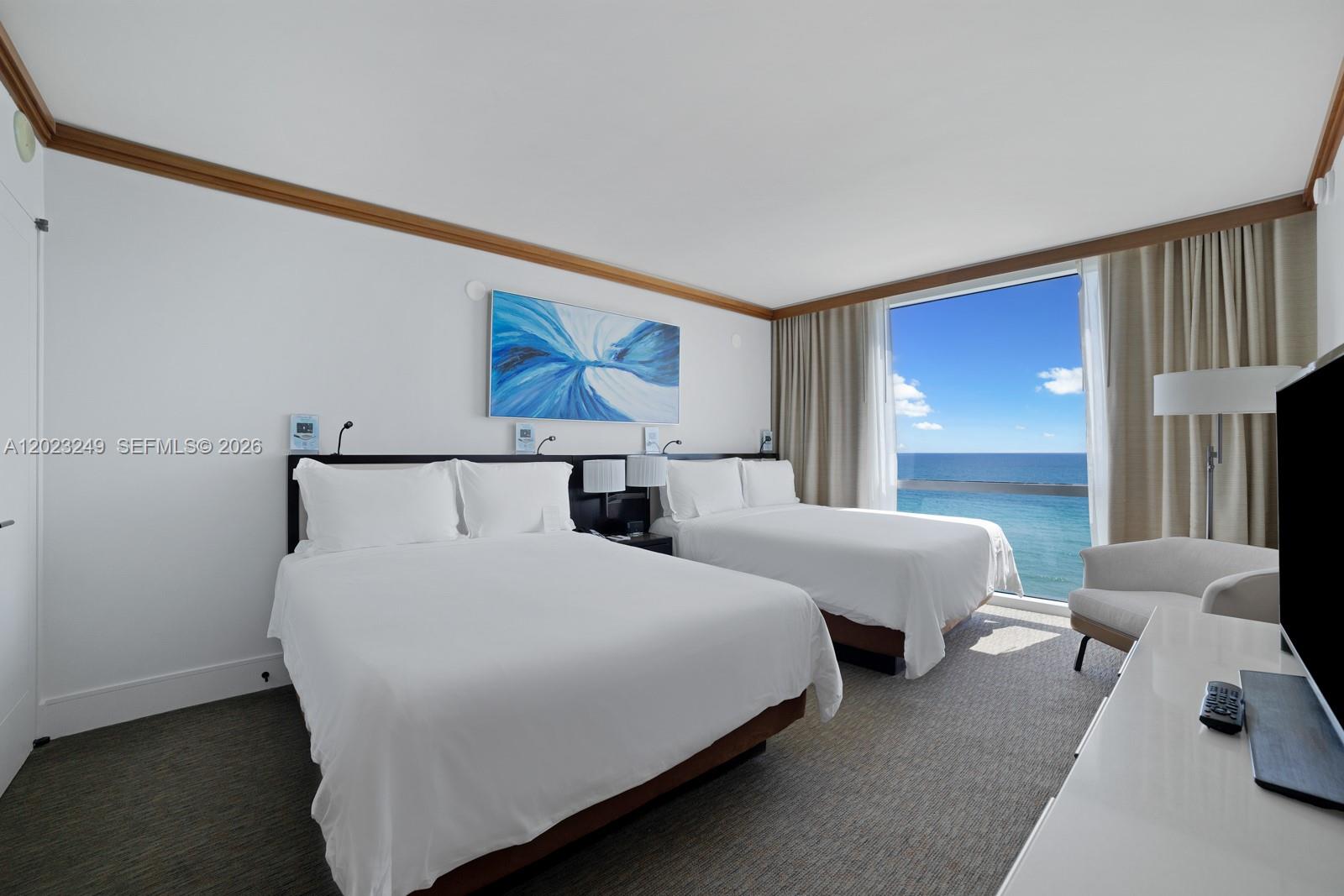 A hotel room features two beds, a large window with ocean views, and white walls — 6801 Collins Ave, Miami Beach FL 33141, MIAMI BEACH, FL