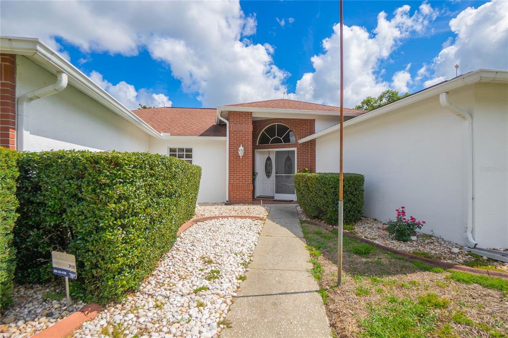 A single-story house exterior features a brick entryway, white stucco walls, and a stone walkway — 3943 W FIELDWOOD COURT, LECANTO, FL